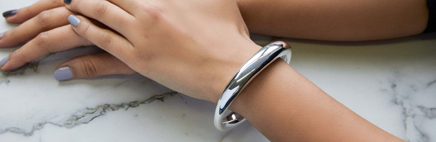 Image of a silver bangle shown on a woman's wrist against a marble background