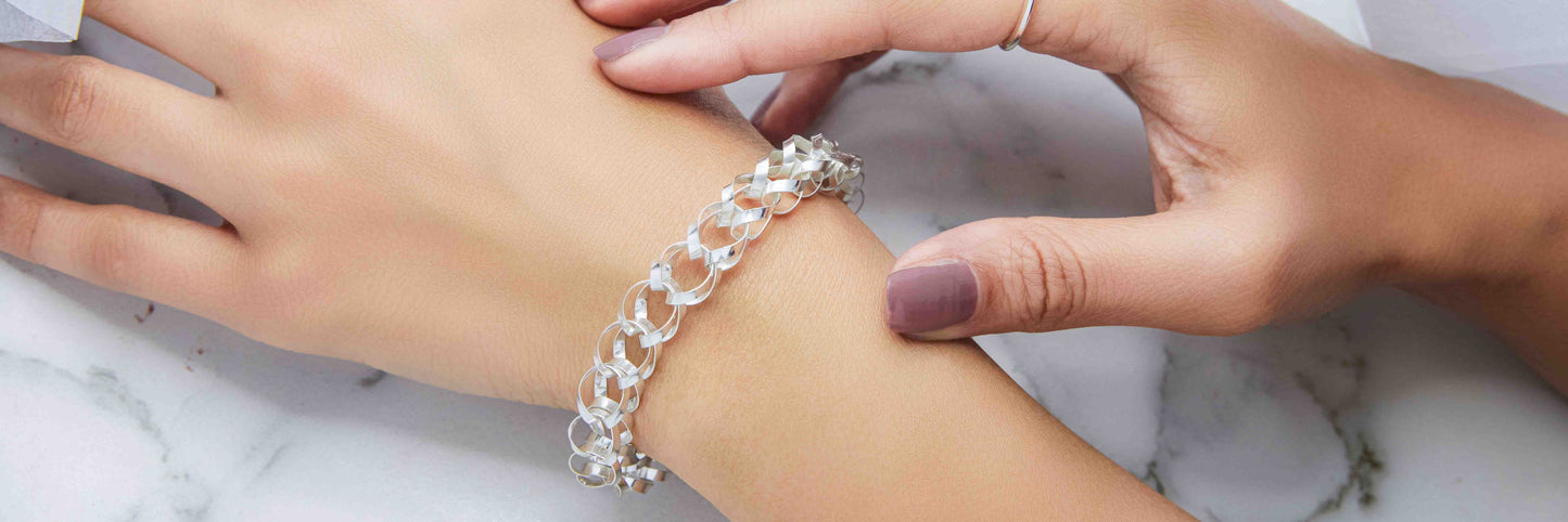 Hand wearing a handcrafted silver chain bracelet from Otis Jaxon’s women’s bracelet collection, styled on a marble background