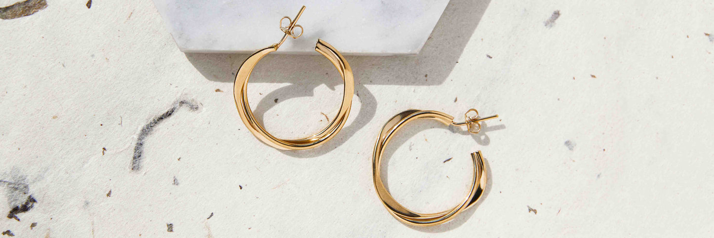 A ppair og gold plated silver hoop earrings on a mottled handmade card background