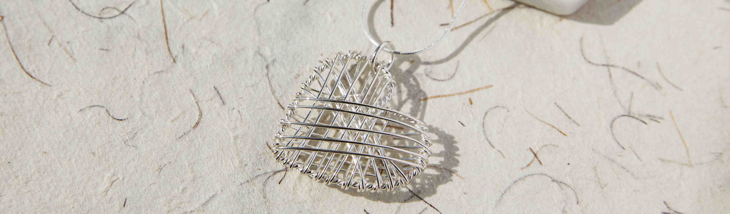 Image of a handmade silver wire heart pendant against a handmade paper background