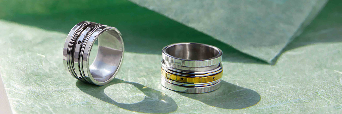 Image of two wide anxiety rings one all silver and one two tone silver and gold against a green background