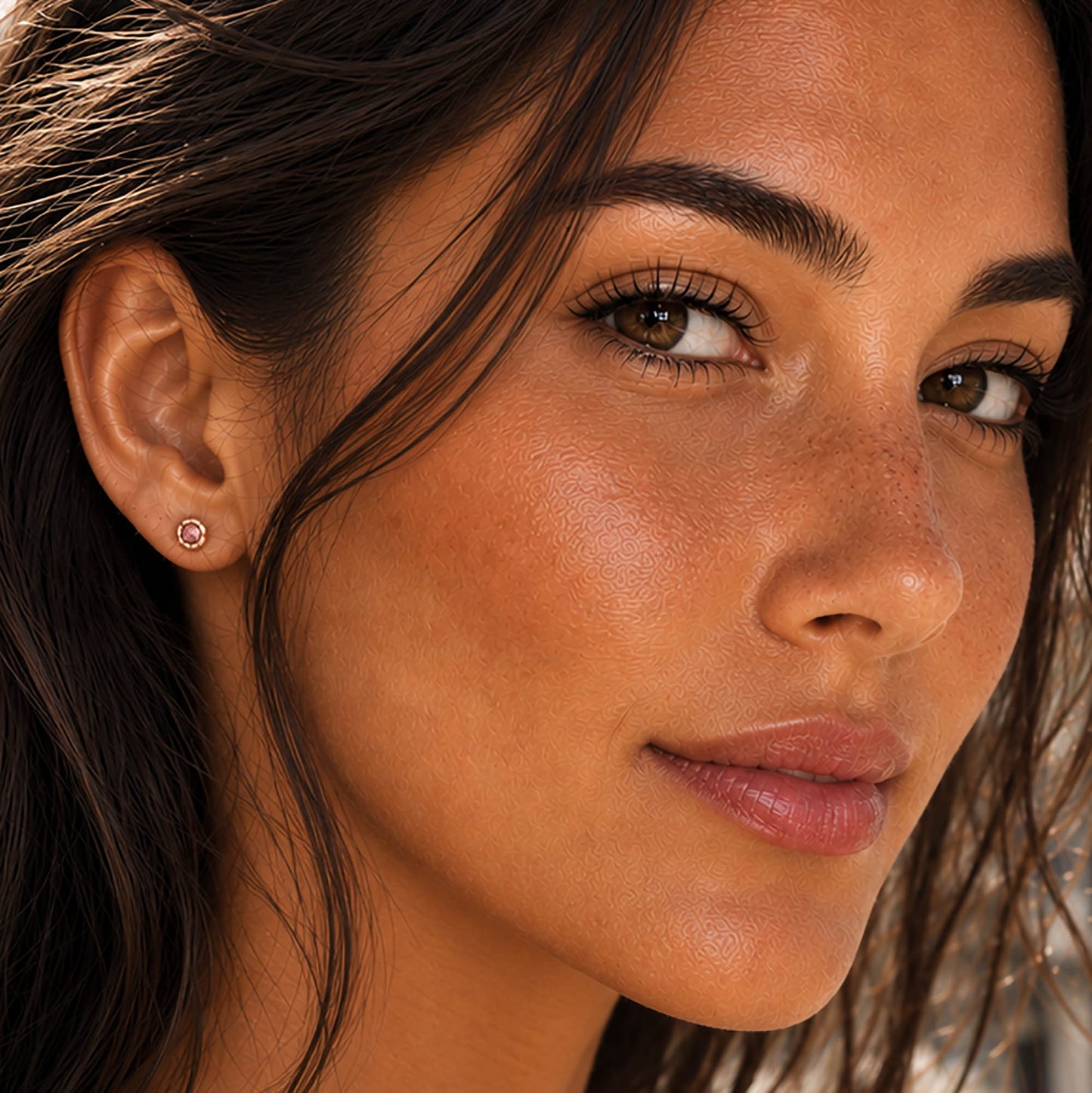 A close-up of a woman's face and ear wearing a small round stud earring with a pink gemstone.